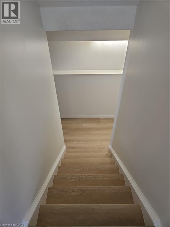 Wood-finish staircase with white risers and baseboards, leading to a light wood-finish flooring area - 390 Wake Robin Crescent, Kitchener, ON - Indoor Photo Showing Other Room