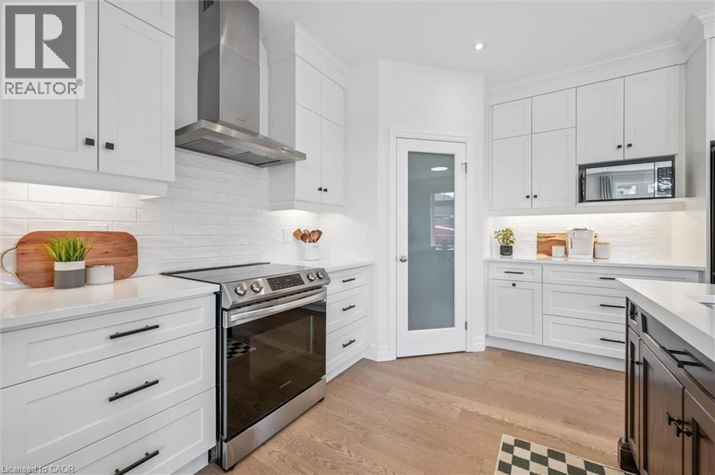 White cabinetry with matte black hardware, stainless steel appliances, light wood-finish flooring, white subway tile backsplash, and frosted glass pantry door - 30 Waterbow Trail, Kitchener, ON - Indoor Photo Showing Kitchen With Upgraded Kitchen