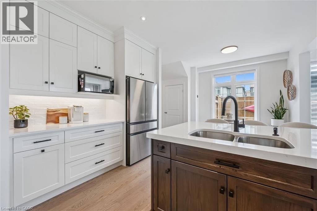 Contemporary kitchen featuring white cabinetry with dark hardware, stainless steel appliances, a white tile backsplash, and wood-finish flooring - 30 Waterbow Trail, Kitchener, ON - Indoor Photo Showing Kitchen With Double Sink