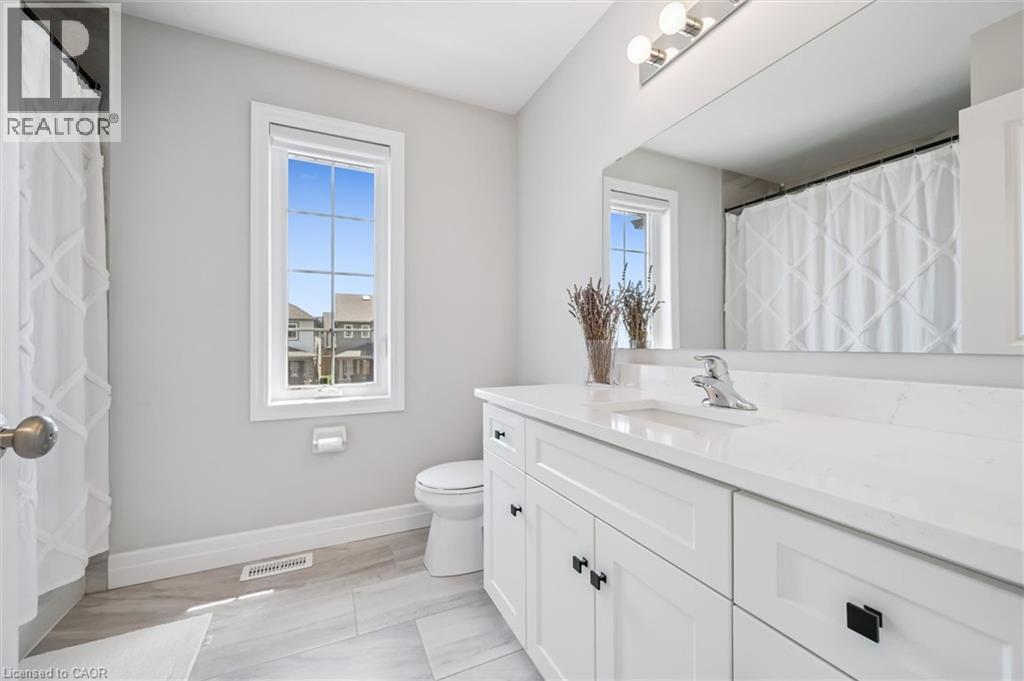 Bathroom featuring a white vanity with black hardware, a polished chrome faucet, a large wall-mounted mirror, and a window with white trim - 30 Waterbow Trail, Kitchener, ON - Indoor Photo Showing Bathroom
