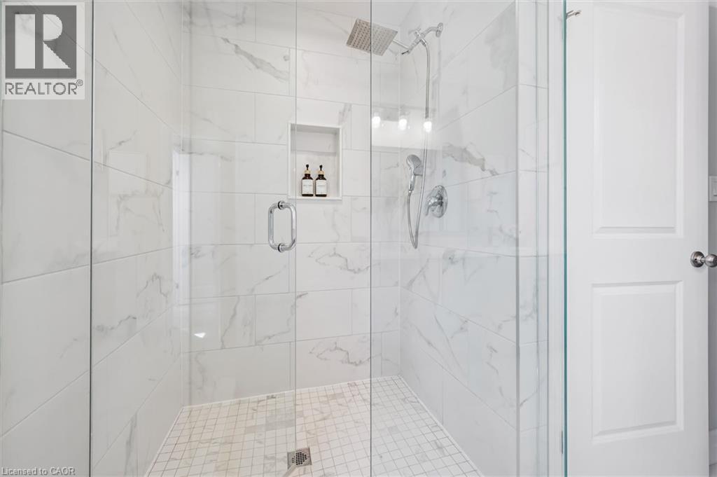 Glass-enclosed shower featuring large format white tile walls with subtle veining, a rain shower head, a handheld shower fixture, and an integrated tiled niche - 30 Waterbow Trail, Kitchener, ON - Indoor Photo Showing Bathroom