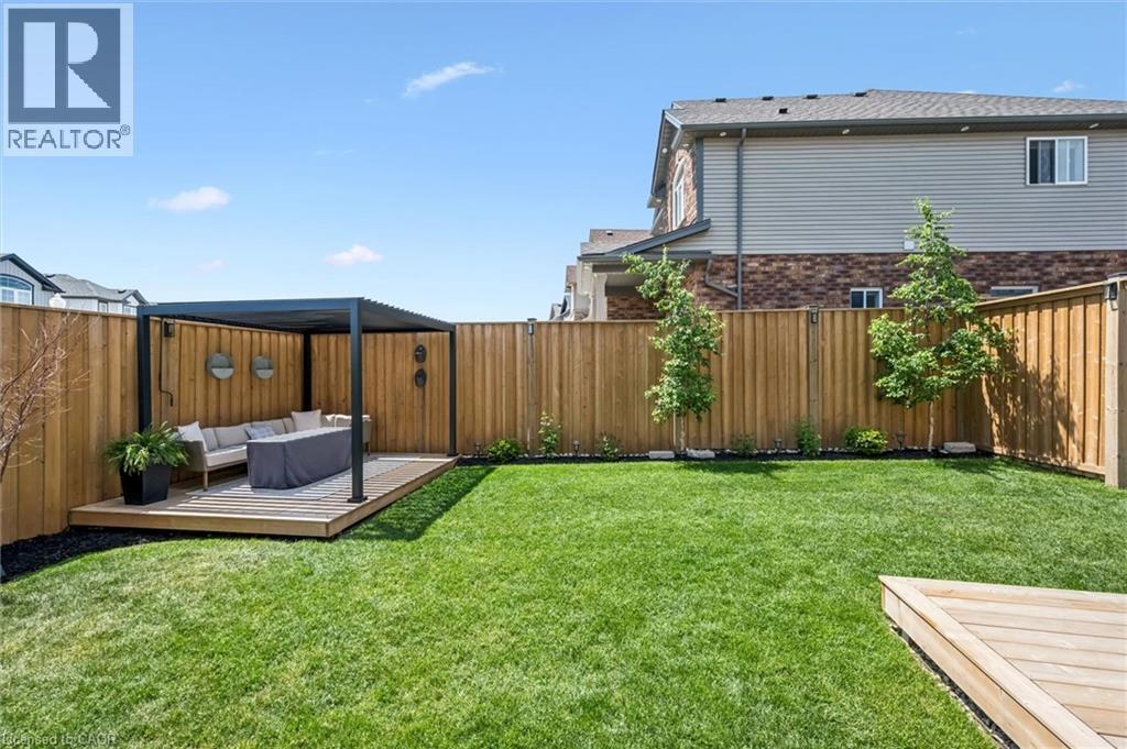 Expansive backyard featuring a lush lawn, privacy fencing, and a built-in wood-finish deck with a contemporary pergola structure - 30 Waterbow Trail, Kitchener, ON - Outdoor With Deck Patio Veranda