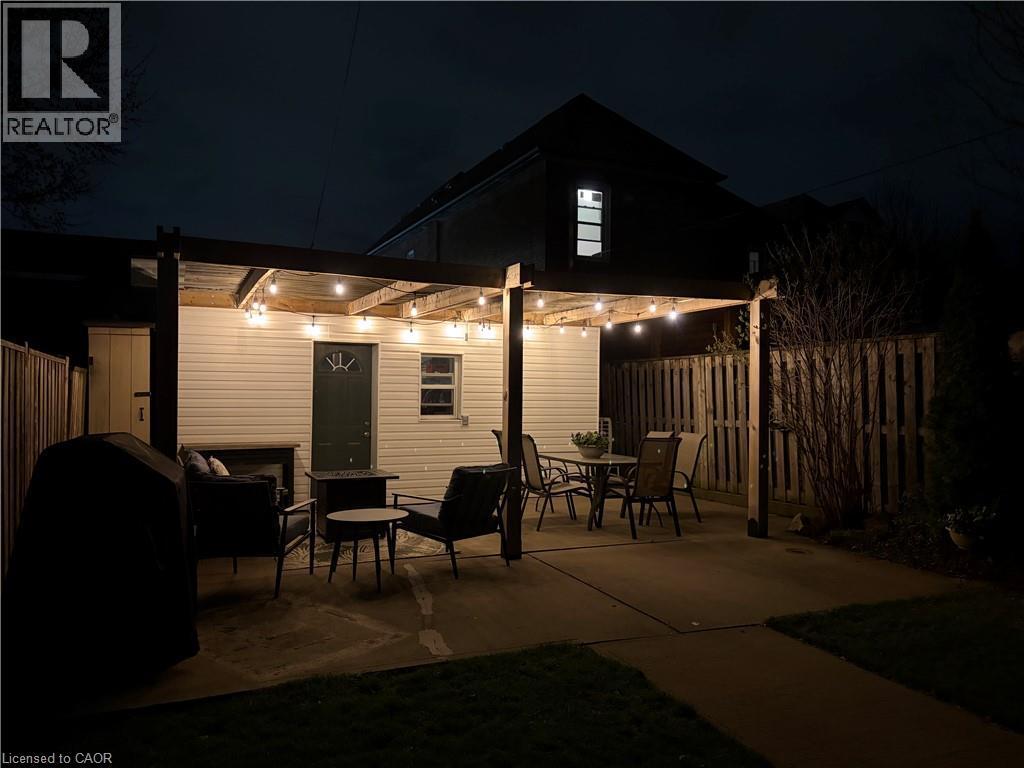 Outdoor patio area featuring a concrete surface, overhead string lighting, and a partial privacy fence - 153 Elgin Street, Hamilton, ON
