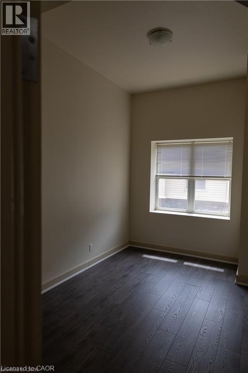 Room featuring dark wood-finish flooring, light neutral-toned walls, a single window with blinds, and an overhead flush-mount light fixture - 365 Colborne Street, Brantford, ON