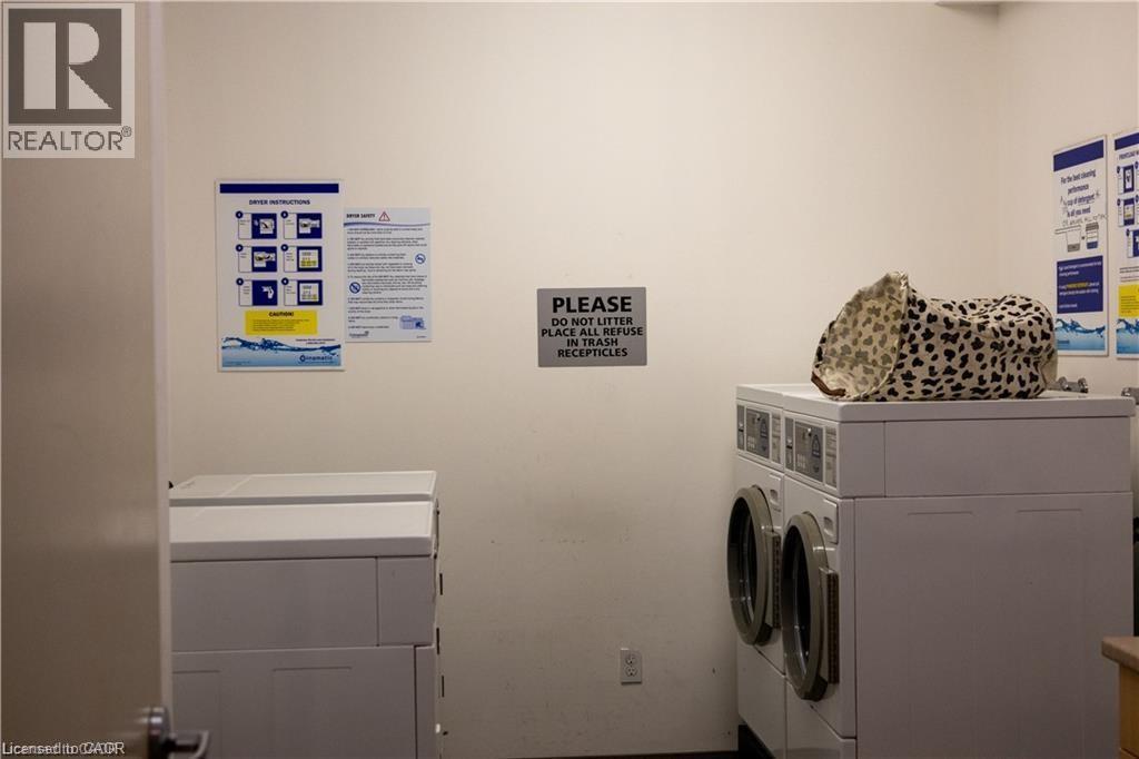 Common area laundry facility with multiple white front-loading washing machines and top-loading dryers - 365 Colborne Street, Brantford, ON