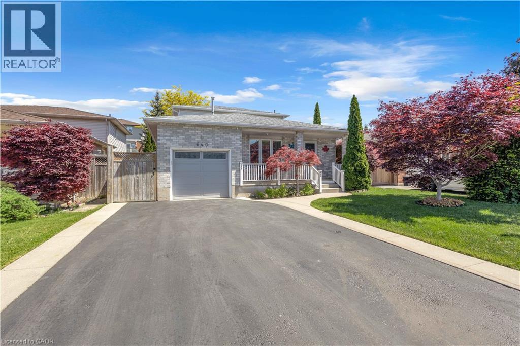 Stone-clad exterior featuring a light gray garage door, a front porch with white railings, and a paved driveway - 640 Acadia Drive, Hamilton, ON
