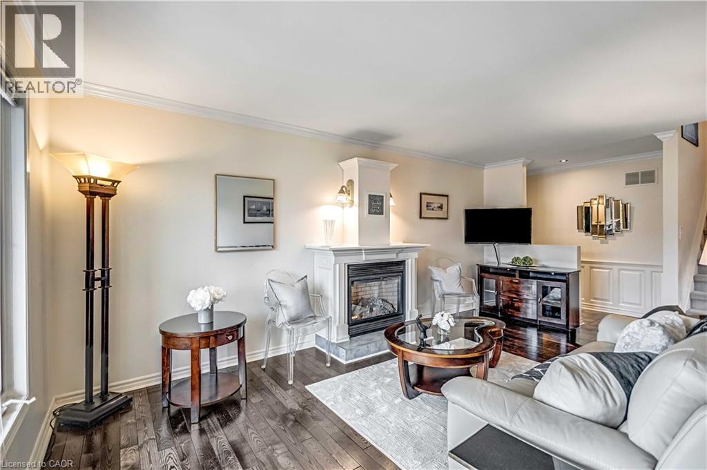Living area featuring rich wood-finish flooring, a contemporary fireplace with a stone surround and white mantel, and crown molding - 640 Acadia Drive, Hamilton, ON