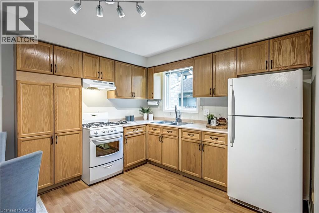 Kitchen featuring wood-finish cabinetry, white appliances, track lighting, and a window above the sink - 640 Acadia Drive, Hamilton, ON