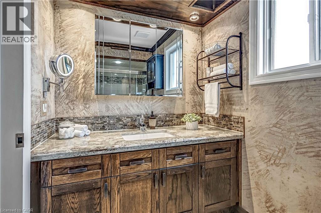 Bathroom vanity featuring a light-toned stone countertop, integrated sink, and wood-finish cabinetry - 640 Acadia Drive, Hamilton, ON