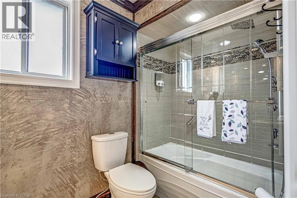 Full bathroom featuring a shower-tub combination with sliding glass enclosure, tile surround with decorative accent band, and recessed lighting - 640 Acadia Drive, Hamilton, ON