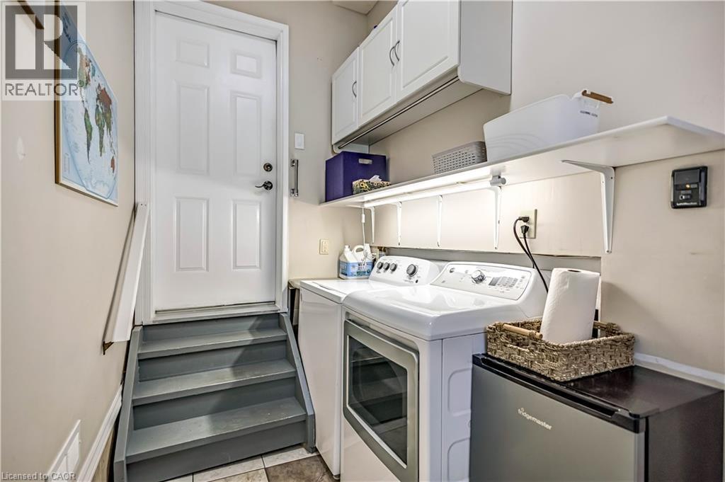 Dedicated laundry area featuring a washer and dryer, upper cabinetry, shelving, and a paneled entry door - 640 Acadia Drive, Hamilton, ON