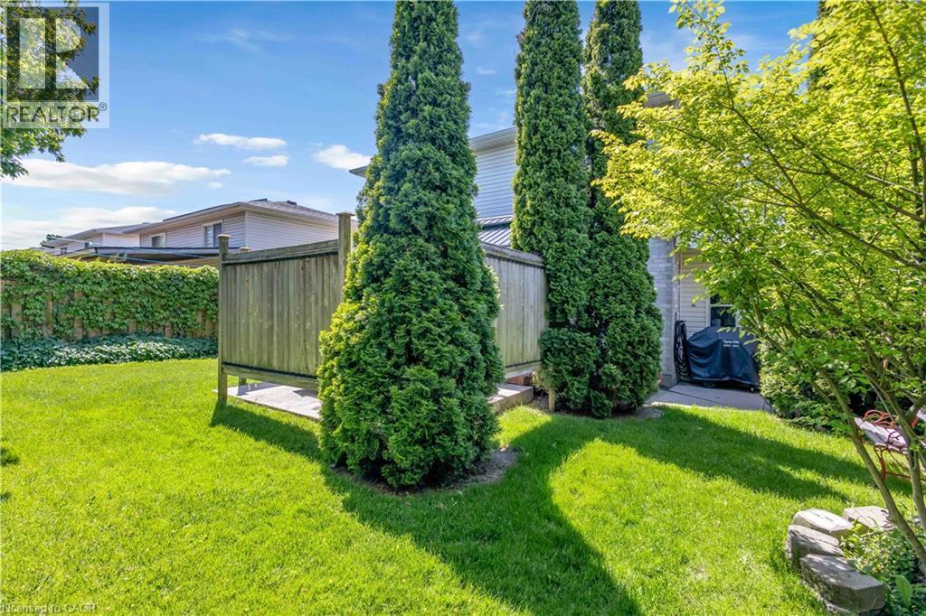 Expansive green lawn featuring a privacy fence, mature trees, and a paved patio area - 640 Acadia Drive, Hamilton, ON