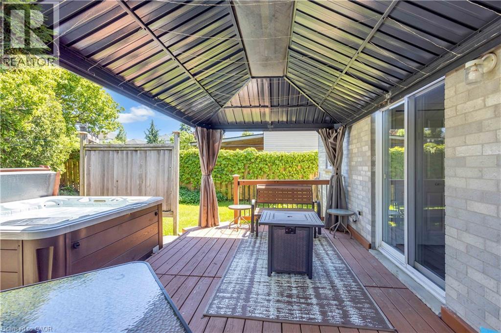 Expansive backyard deck featuring a dark composite surface, a built-in hot tub, and a covered pergola - 640 Acadia Drive, Hamilton, ON