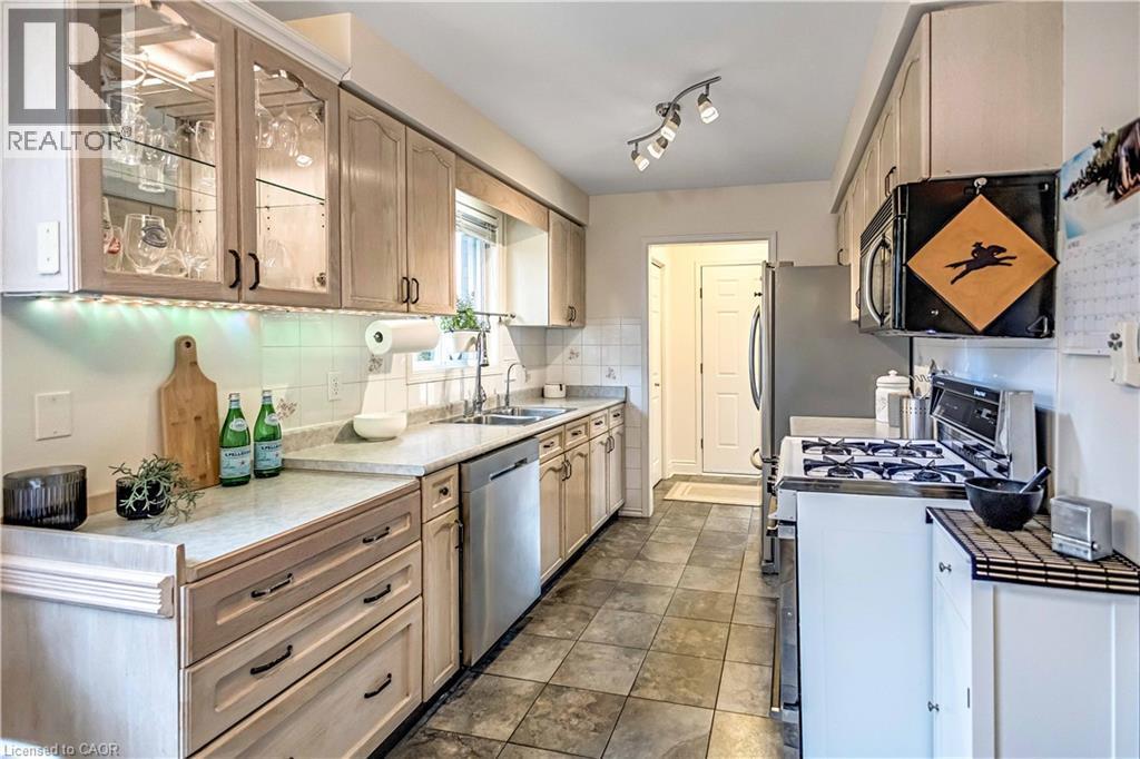 Galley kitchen with light wood-finish cabinetry, a window over the sink, and tile flooring - 640 Acadia Drive, Hamilton, ON