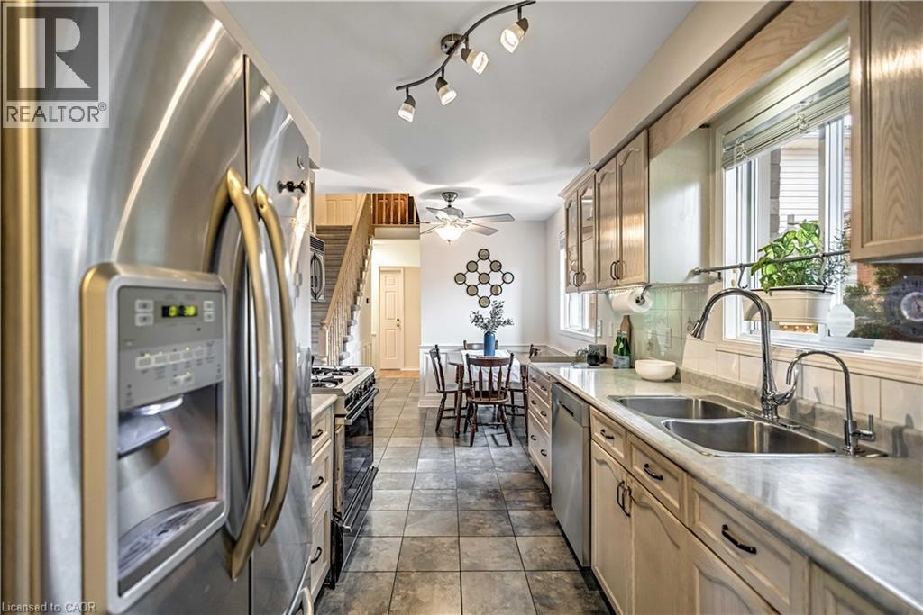 Galley kitchen with stainless steel appliances, light wood-finish cabinetry, a double basin sink, and tile flooring - 640 Acadia Drive, Hamilton, ON
