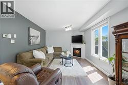 Living area featuring wood-finish flooring, a corner fireplace with a white mantel, and a large window with white trim -