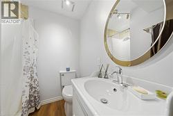 Bathroom with wood-finish flooring, a white vanity with integrated sink, and a circular mirror with a gold-toned frame -