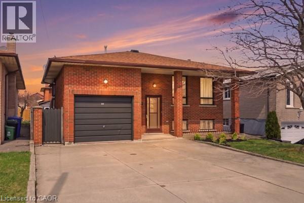 Brick exterior featuring a private driveway, attached garage, covered entryway, and mature landscaping - 957 Stone Church Road E, Hamilton, ON - Outdoor