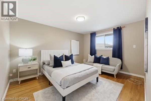 Spacious room featuring wood-finish flooring, a contemporary ceiling light fixture, and a window with dark curtains - 957 Stone Church Road E, Hamilton, ON - Indoor Photo Showing Bedroom