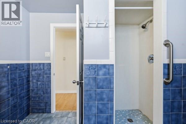 Shower stall with white surround and mosaic tile flooring, featuring a wall-mounted showerhead and grab bar - 957 Stone Church Road E, Hamilton, ON - Indoor Photo Showing Bathroom