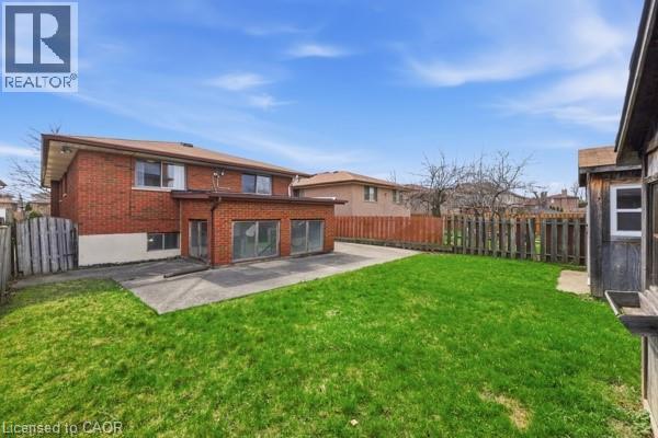 Spacious rear yard featuring an expansive lawn, concrete patio, and mature perimeter fencing - 957 Stone Church Road E, Hamilton, ON - Outdoor