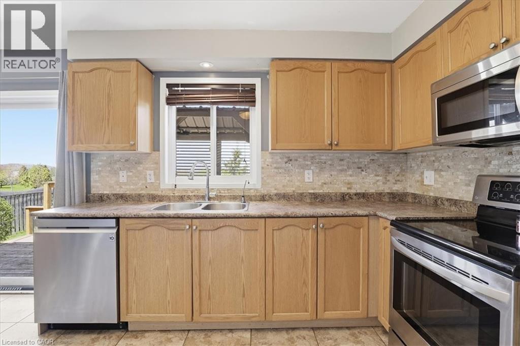 Kitchen featuring oak-finish cabinetry, stainless steel appliances, a double basin sink, mosaic tile backsplash, and durable countertops - 136 Carpenter Road, Cambridge, ON - Indoor Photo Showing Kitchen