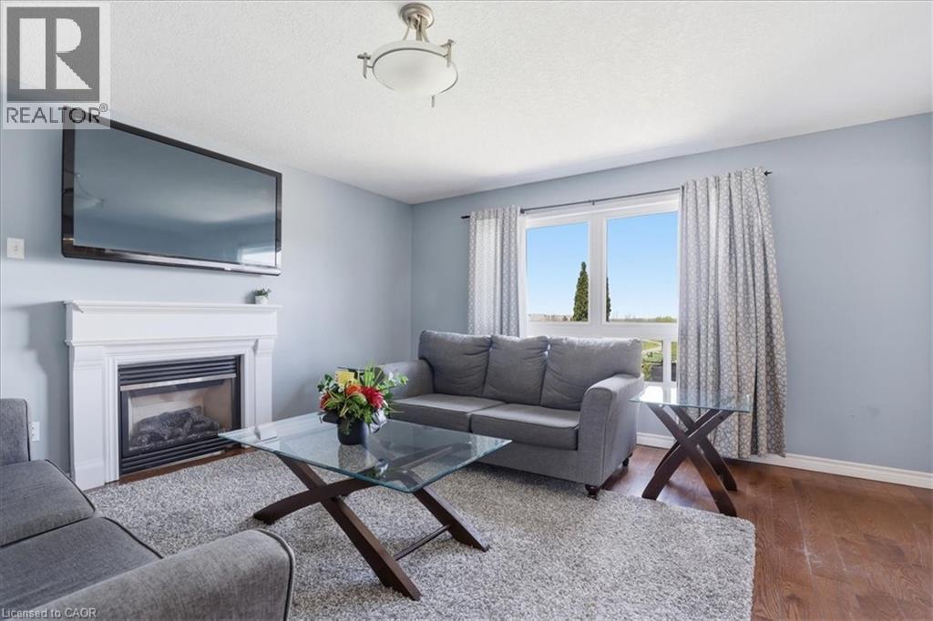Living area featuring a fireplace with a white mantel, a large window with patterned drapes, a ceiling-mounted light fixture, and wood-finish flooring - 136 Carpenter Road, Cambridge, ON - Indoor Photo Showing Living Room With Fireplace