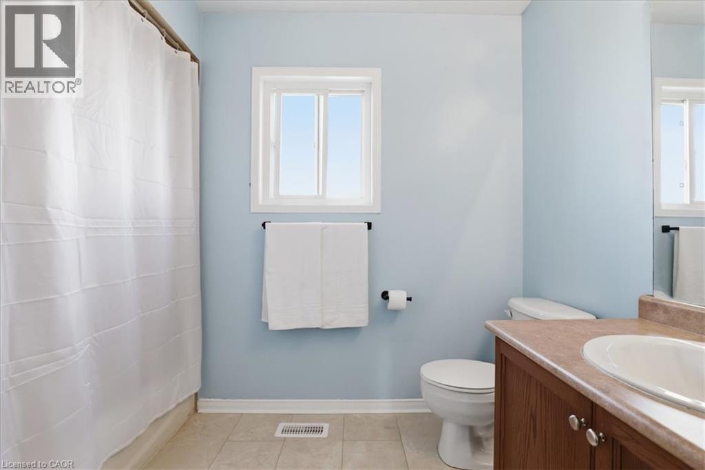 Bathroom with a window, white shower curtain, tiled flooring, wood-finish vanity with a countertop, and an oval sink - 136 Carpenter Road, Cambridge, ON - Indoor Photo Showing Bathroom