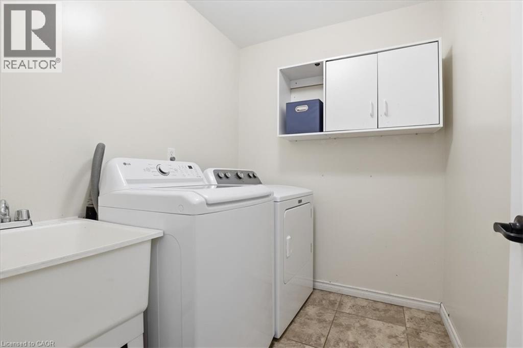 Dedicated laundry area featuring a utility sink with a two-handle faucet, wall-mounted cabinetry with an open shelf, and neutral-toned wall paint - 136 Carpenter Road, Cambridge, ON - Indoor Photo Showing Bathroom