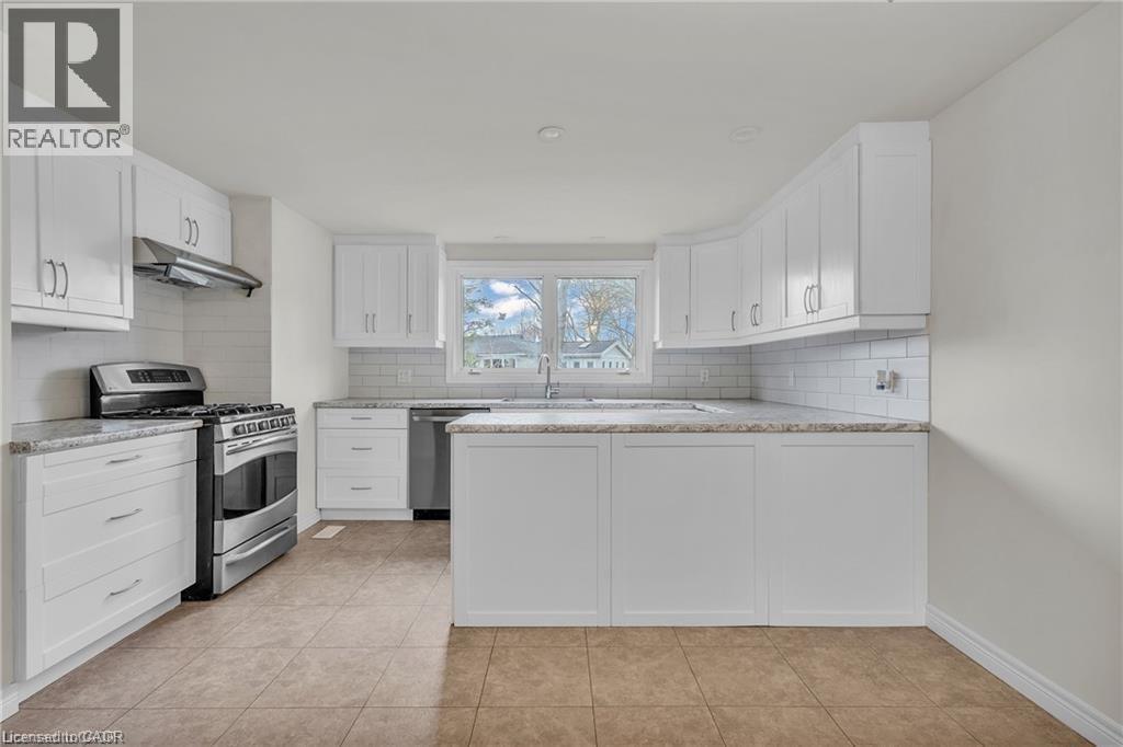 Open-concept kitchen featuring white cabinetry, subway tile backsplash, stainless steel appliances, granite countertops, and tile flooring - 22 Blackhorne Crescent, Kitchener, ON - Indoor Photo Showing Kitchen