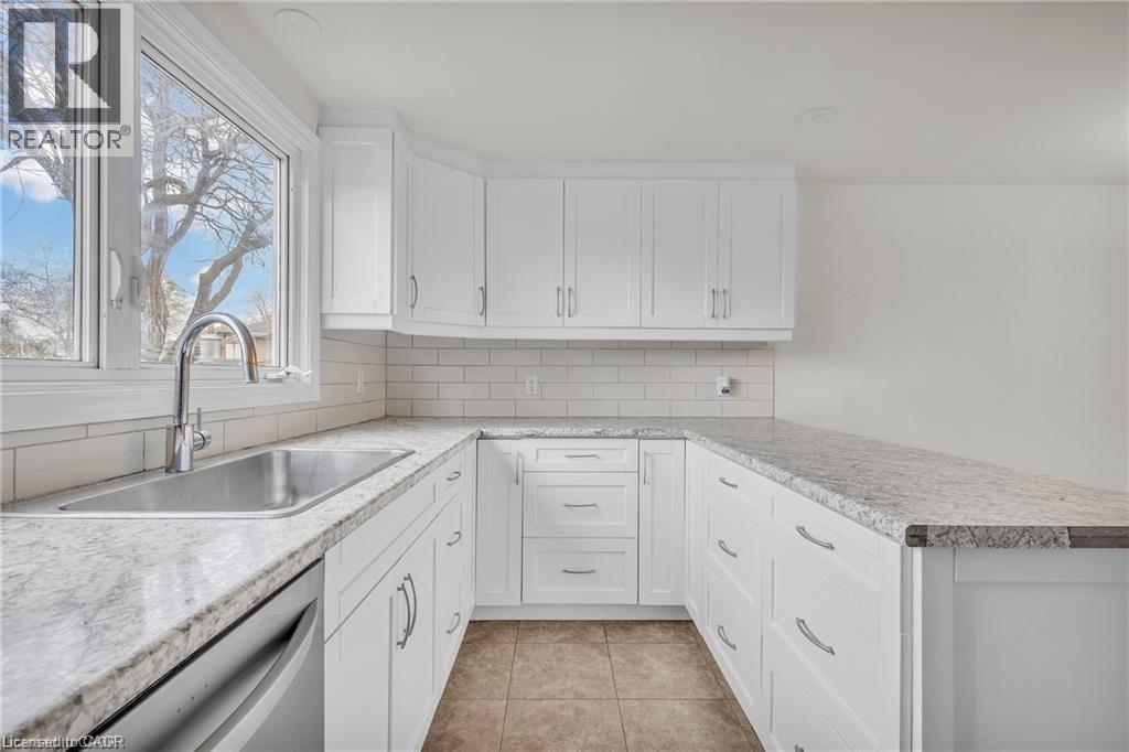 Bright kitchen featuring white shaker cabinetry, speckled countertops, stainless steel undermount sink with gooseneck faucet, subway tile backsplash, and tile flooring - 22 Blackhorne Crescent, Kitchener, ON - Indoor Photo Showing Kitchen With Upgraded Kitchen