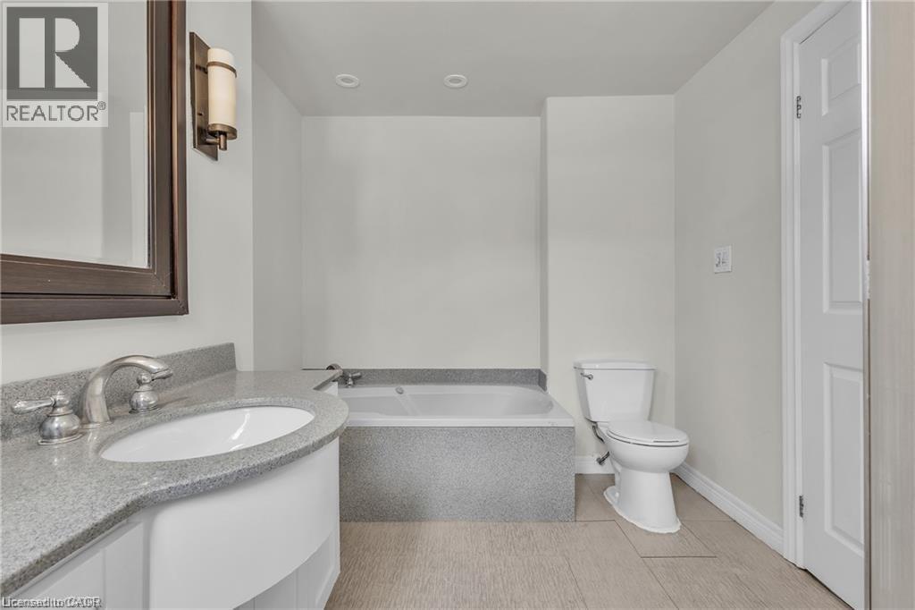 Bathroom featuring a built-in tub, white vanity with a gray speckled countertop, undermount sink, and recessed lighting - 22 Blackhorne Crescent, Kitchener, ON - Indoor Photo Showing Bathroom