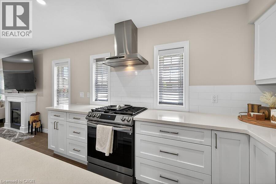 Kitchen featuring a stainless steel range with overhead ventilation, white shaker cabinetry, light-toned countertops, and a white subway tile backsplash - 109 Ray Street N, Hamilton, ON - Indoor Photo Showing Kitchen With Upgraded Kitchen