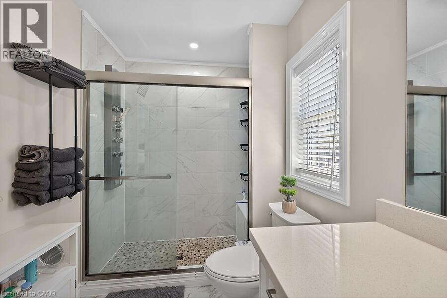 Contemporary bathroom featuring a glass-enclosed shower with tile surround and pebble flooring, a white window with blinds, and a light-toned countertop - 109 Ray Street N, Hamilton, ON - Indoor Photo Showing Bathroom