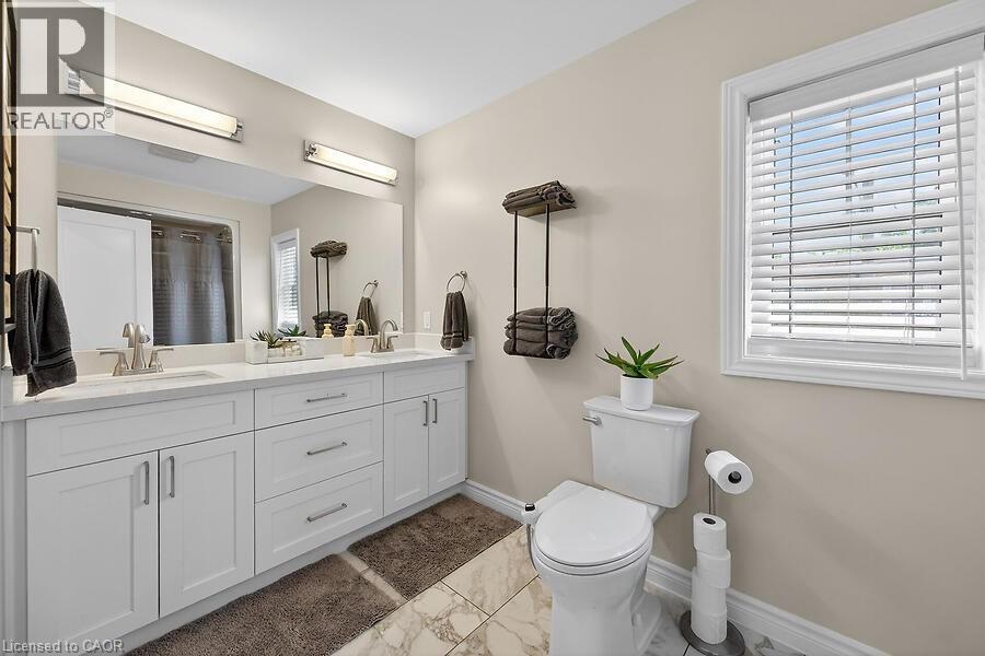 Dual vanity with undermount sinks and chrome fixtures, set against a large mirror with two overhead light bars - 109 Ray Street N, Hamilton, ON - Indoor Photo Showing Bathroom