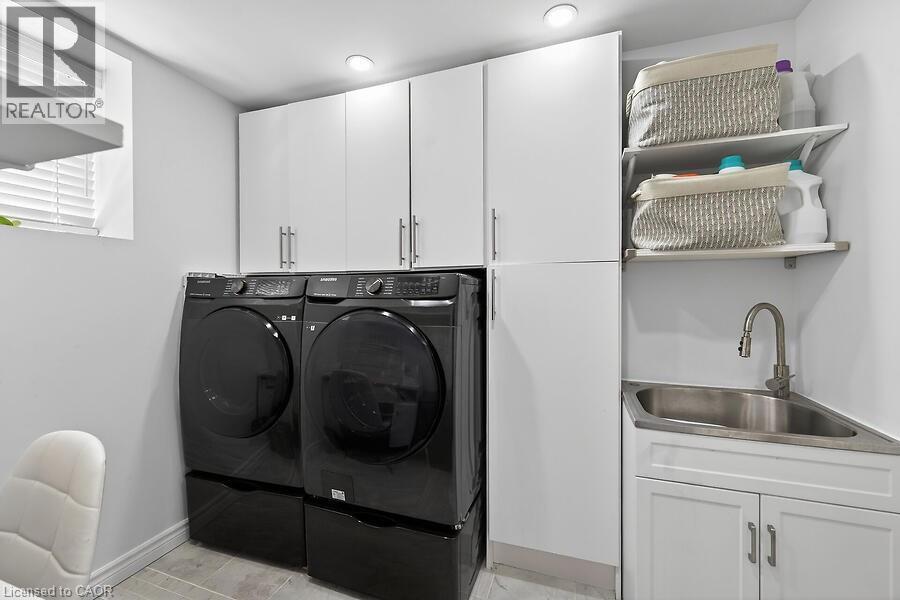 Dedicated laundry area featuring white cabinetry, a utility sink with a gooseneck faucet, and integrated shelving - 109 Ray Street N, Hamilton, ON - Indoor Photo Showing Laundry Room