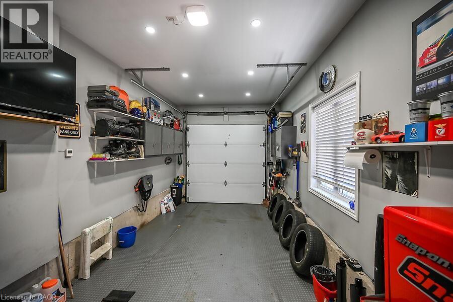 Attached garage featuring a white overhead door, multiple recessed lights, built-in shelving, a window with blinds, and a wall-mounted television - 109 Ray Street N, Hamilton, ON - Indoor Photo Showing Garage