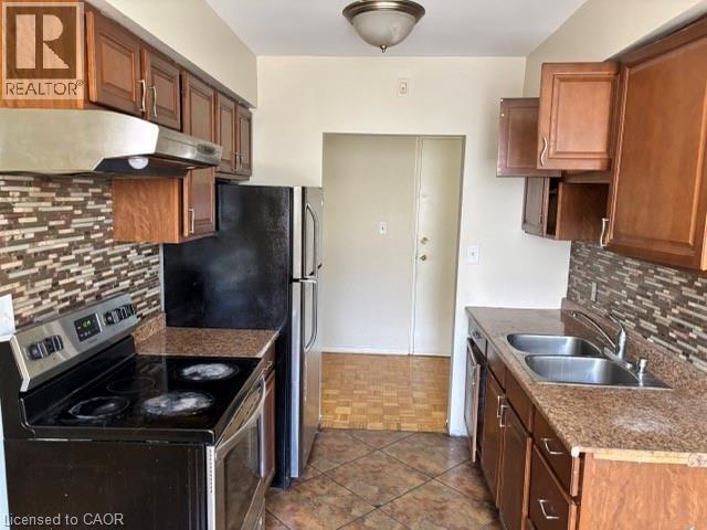 Kitchen featuring warm wood cabinetry, granite-style countertops, mosaic tile backsplash, and stainless steel sink - 2205 King Street E Unit# 1, Hamilton, ON - Indoor Photo Showing Kitchen With Double Sink