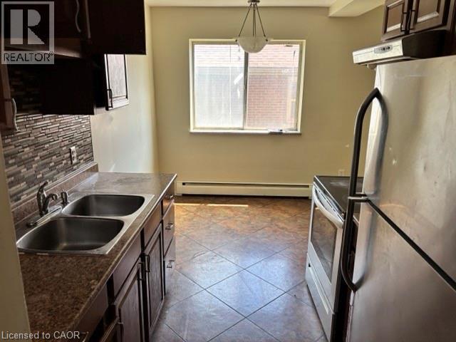 Kitchen featuring dark wood cabinetry, a double basin stainless steel sink, and a multi-toned tile backsplash - 2205 King Street E Unit# 1, Hamilton, ON - Indoor Photo Showing Kitchen With Double Sink