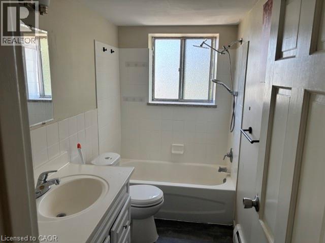 Bathroom featuring a full bathtub with tile surround, a single vanity with an integrated sink, a built-in medicine cabinet, and a window providing natural light - 2205 King Street E Unit# 1, Hamilton, ON - Indoor Photo Showing Bathroom