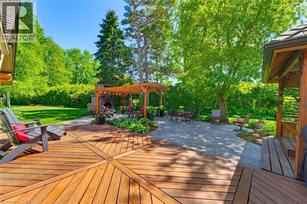Expansive backyard featuring a radial-pattern wood deck, a stone patio, a wooden pergola, a stone fireplace, and a covered wooden structure - 169 James Street, Atwood, ON - Outdoor With Deck Patio Veranda With Backyard