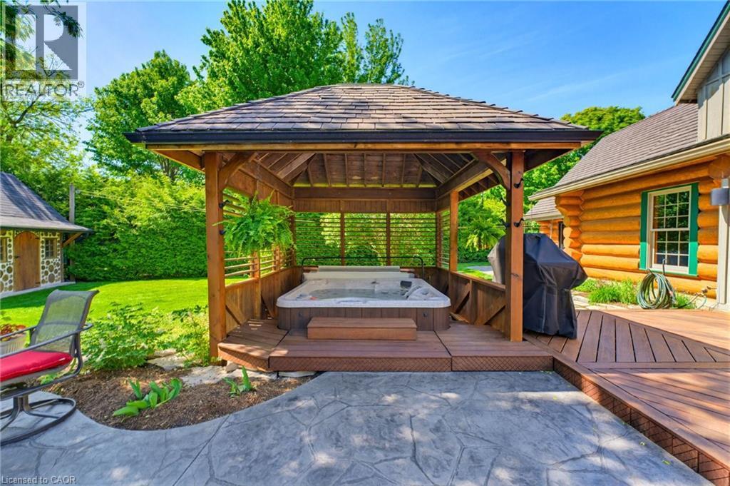 Covered outdoor spa area with a wood pergola, integrated hot tub, multi-level wood decking, and stamped concrete patio - 169 James Street, Atwood, ON - Outdoor With Deck Patio Veranda With Exterior