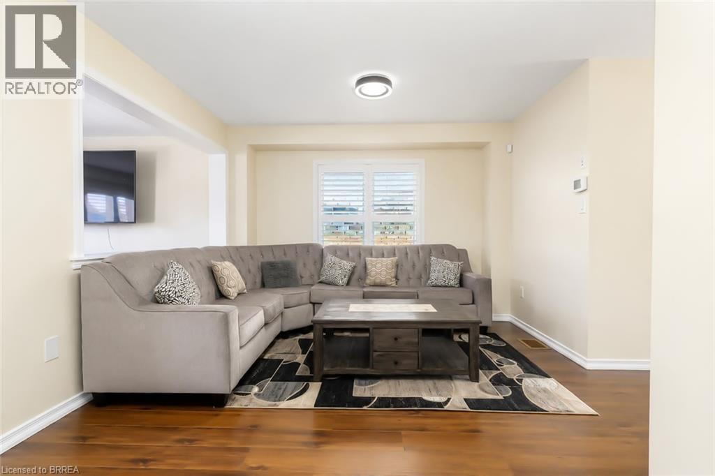 Bright living area featuring wood-finish flooring, light-toned walls, and a window with white shutters - 26 Pollard Street, Brantford, ON - Indoor Photo Showing Living Room