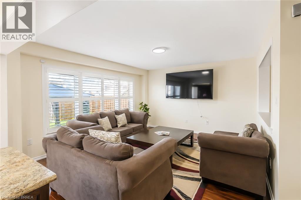 Spacious living area featuring wood-finish flooring, light neutral wall tones, and a large window with white louvered blinds - 26 Pollard Street, Brantford, ON - Indoor Photo Showing Living Room