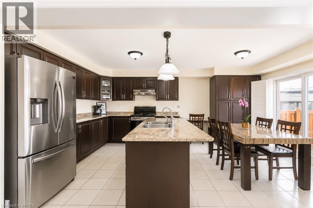 Open-concept kitchen featuring dark wood cabinetry, stainless steel appliances, light-toned countertop surfaces, a kitchen island with an integrated sink, and white tile flooring - 26 Pollard Street, Brantford, ON - Indoor