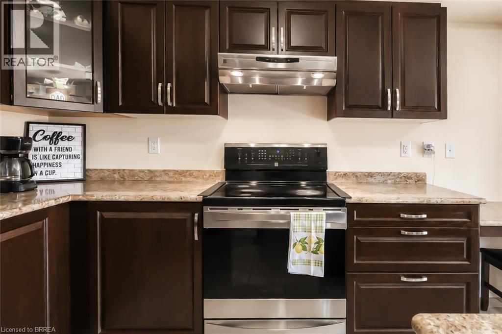Modern kitchen featuring dark wood cabinetry, light-toned countertops, and a built-in stainless steel range with a coordinating range hood - 26 Pollard Street, Brantford, ON - Indoor Photo Showing Kitchen