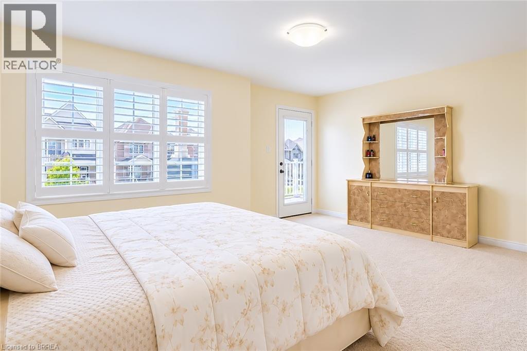 Bright room featuring a triple window with white plantation shutters, a glass-paneled exterior door leading to a balcony, and light-toned wall-to-wall carpeting - 26 Pollard Street, Brantford, ON - Indoor Photo Showing Bedroom