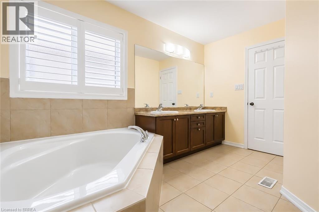 Bathroom featuring a built-in corner bathtub, plantation shutters, a dual sink vanity with brown cabinetry, a large mirror, and tile flooring - 26 Pollard Street, Brantford, ON - Indoor Photo Showing Bathroom