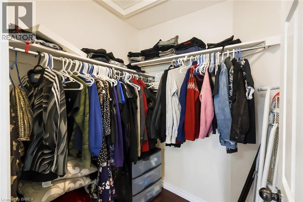 Walk-in closet featuring white perimeter shelving, multiple hanging rods, and wood-finish flooring - 26 Pollard Street, Brantford, ON - Indoor With Storage