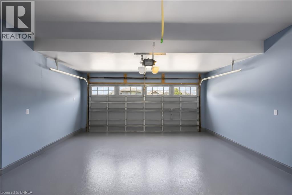 Spacious garage featuring a durable gray epoxy floor, light blue painted walls, an automatic garage door opener, and a garage door with upper window panels - 26 Pollard Street, Brantford, ON - Indoor Photo Showing Garage
